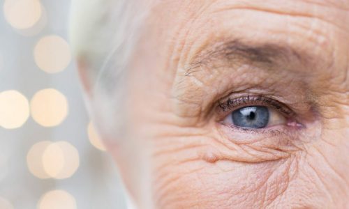 age, vision and old people concept - close up of senior woman face and eye over holidays lights background